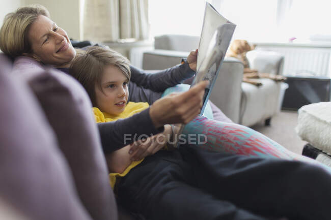 Happy mother and son reading book on living room sofa — Stock Photo