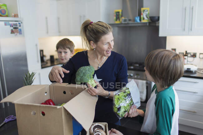 Мать и сыновья выгружают свежие продукты из коробки на кухню — стоковое фото