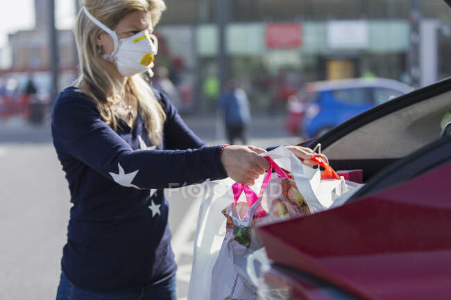Mulher em máscara facial carregando mantimentos no carro — Fotografia de Stock