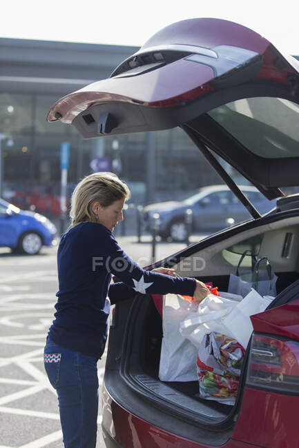 Женщина загружает продукты в багажник автомобиля на парковке — стоковое фото