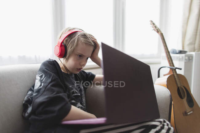 Boy with headphones and laptop on living room sofa — Stock Photo