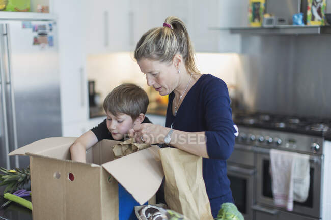 Madre e figlio scarico prodotti dalla scatola in cucina — Foto stock