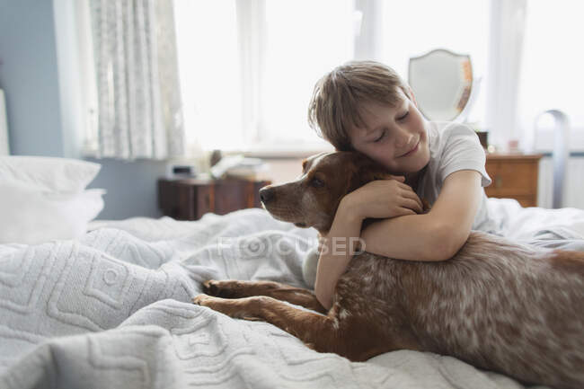 Милый мальчик обнимает собаку на кровати — стоковое фото