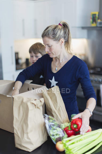 Madre e figlio che scaricano prodotti freschi in cucina — Foto stock