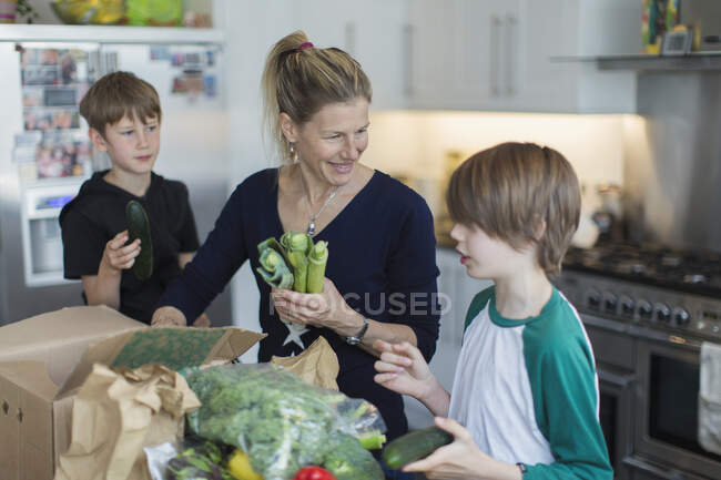 Felice madre e figli che scaricano prodotti freschi dalla scatola in cucina — Foto stock