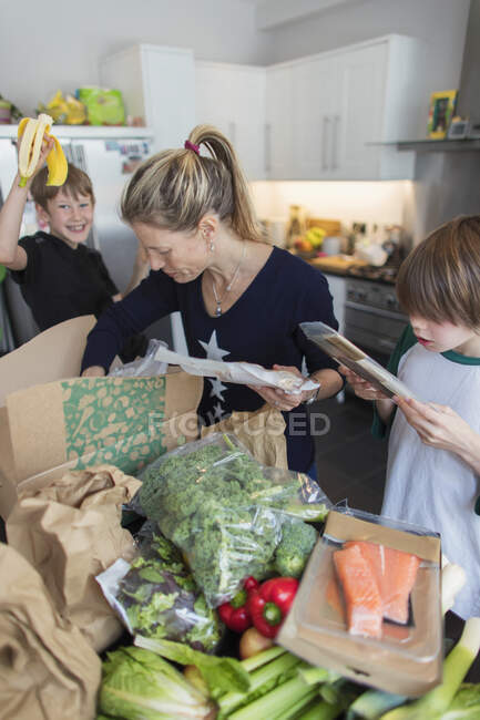 Mujer e hijos descargando productos frescos de la caja en la cocina - foto de stock