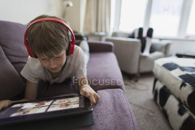 Мальчик с наушниками и цифровыми планшетами домашнее обучение на диване — стоковое фото