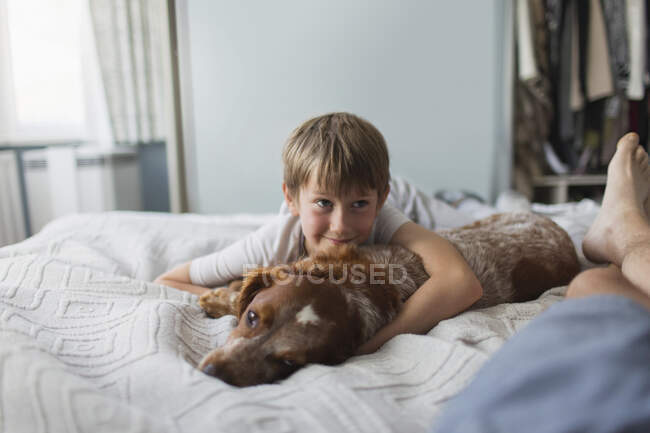 Cute boy cuddling with dog on bed — Stock Photo