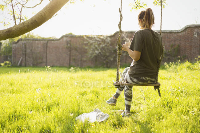 Femme avec café sur balançoire dans un jardin ensoleillé — Photo de stock