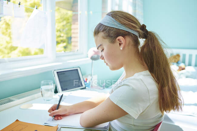 Зачарованная девочка выполняет домашнюю работу за столом в спальне — стоковое фото