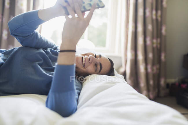 Heureuse adolescente utilisant un téléphone intelligent sur le lit — Photo de stock