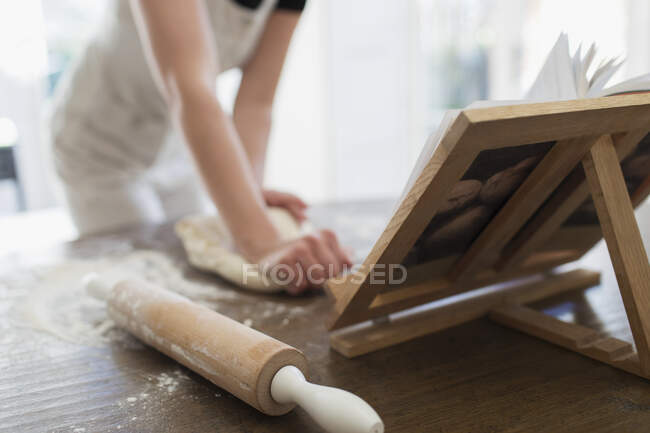 Femme pétrissant la pâte au livre de cuisine — Photo de stock