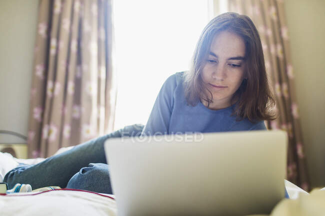 Teenage girl using laptop on bed in sunny bedroom — Stock Photo