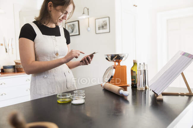 Adolescente chica con teléfono inteligente hornear en la cocina - foto de stock
