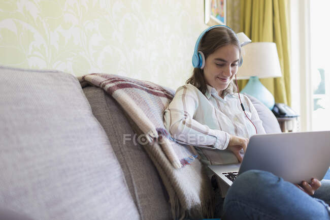 Adolescente avec écouteurs utilisant un ordinateur portable sur le canapé — Photo de stock