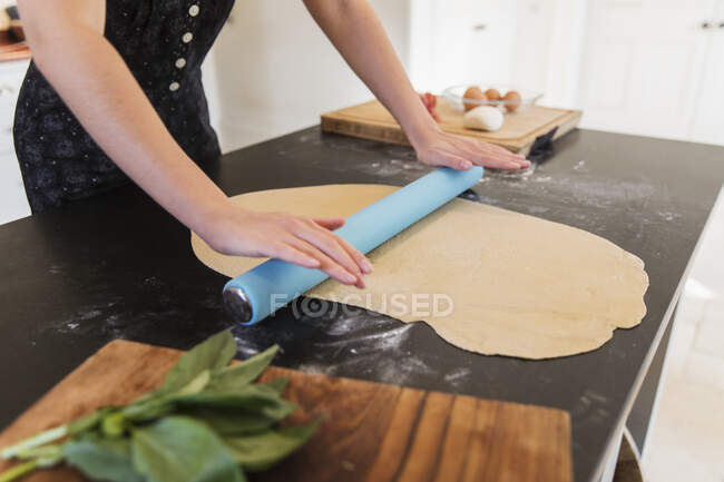 Дівчина-підліток розкачує тісто на кухонній лічильнику — стокове фото