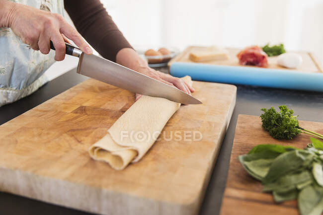 Woman cutting fresh homemade pasta on cutting board — Stock Photo