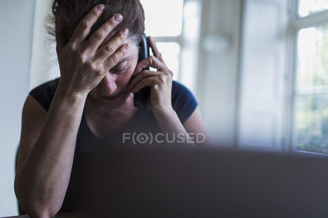 Frustrated woman talking on telephone at laptop — Stock Photo