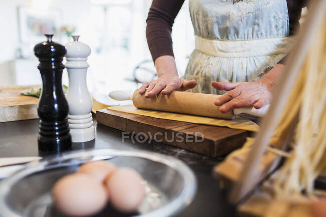 Pâte à rouler femme avec rouleau à pâtisserie dans la cuisine — Photo de stock