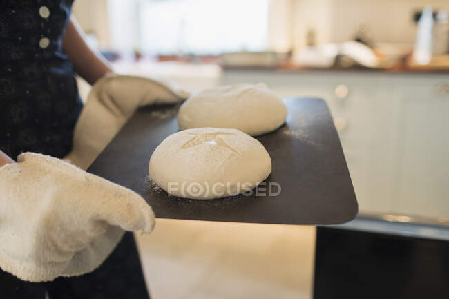 Close up woman with homemade bread dough on tray in kitchen — Stock Photo