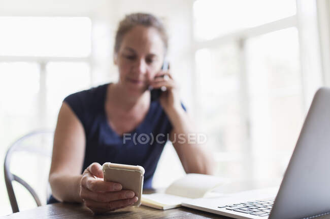 Жінка розмовляє по телефону і використовує смартфон вдома — стокове фото