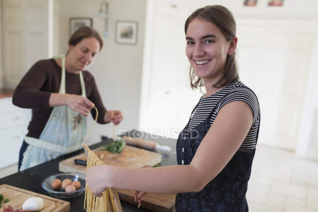 Портрет щаслива дівчина-підліток робить домашню пасту з матір'ю вдома — стокове фото