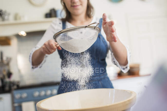 Teenage girl sifting flour in kitchen — Stock Photo
