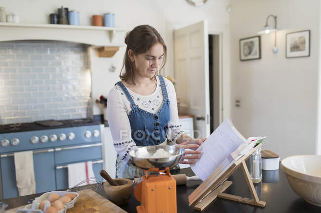 Дівчина-підліток з кулінарною книгою випічка на кухні — стокове фото