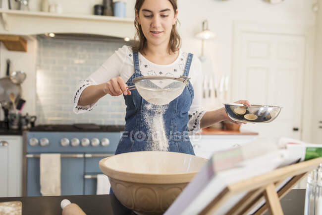 Девочка-подросток просеивает муку для выпечки на кухне — стоковое фото