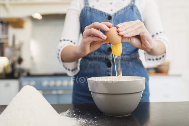 Дівчинка-підліток розбиває яйце в миску для випічки на кухні — стокове фото