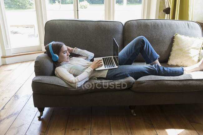 Teenage girl with headphones and laptop video chatting on living room sofa — Stock Photo