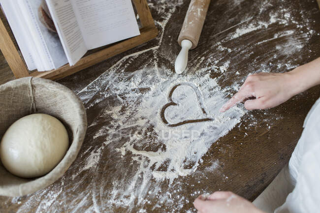 Teenage girl drawing heart shape in flour on kitchen counter — Stock Photo