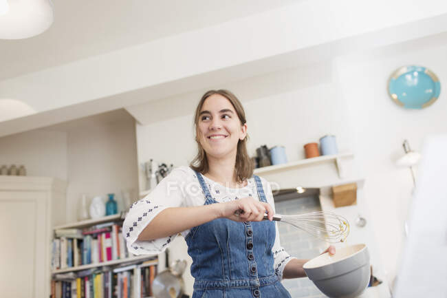 Sorridente ragazza adolescente con frusta e ciotola cottura in cucina — Foto stock