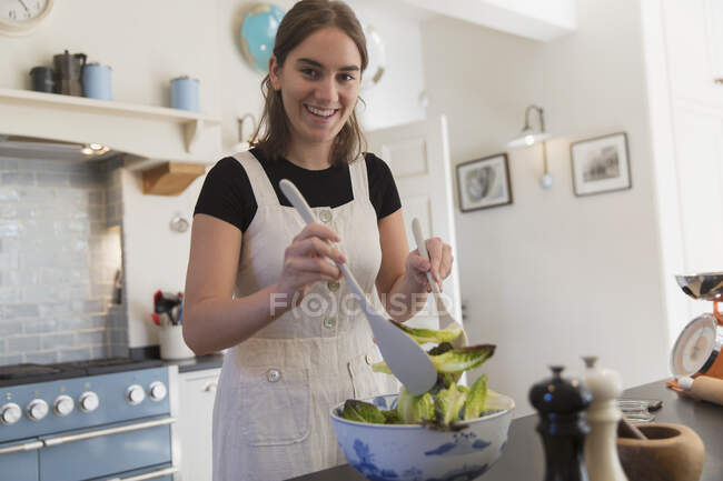 Portrait confident teenage girl making salad in kitchen — Stock Photo