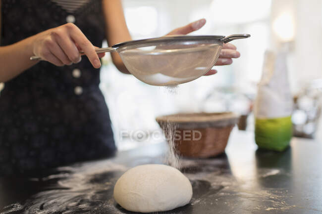 Закрыть женщину просеивая муку хлебного теста на кухонном столе — стоковое фото