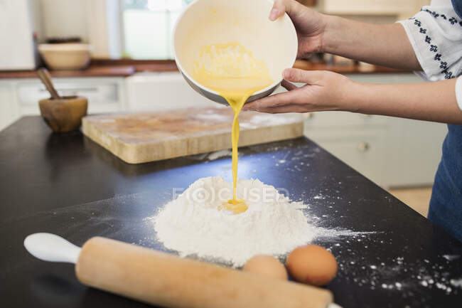 Teenage girl pouring egg yolks into flour nest on kitchen counter — Stock Photo