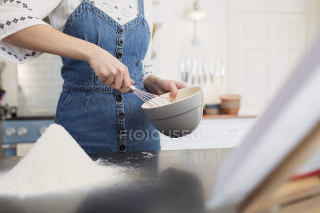 Teenage girl with whisk and bowl baking in kitchen — Stock Photo