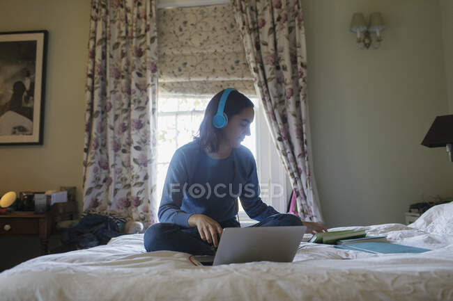 Дівчина-підліток з навушниками та ноутбуком навчається на ліжку — стокове фото