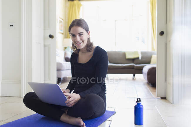 Portrait smiling teenage girl practicing online yoga with laptop at home — Stock Photo