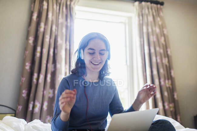 Feliz adolescente con auriculares y portátil escuchando música en la cama - foto de stock
