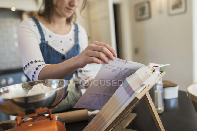 Дівчина-підліток з кулінарною книгою випічка на кухні — стокове фото