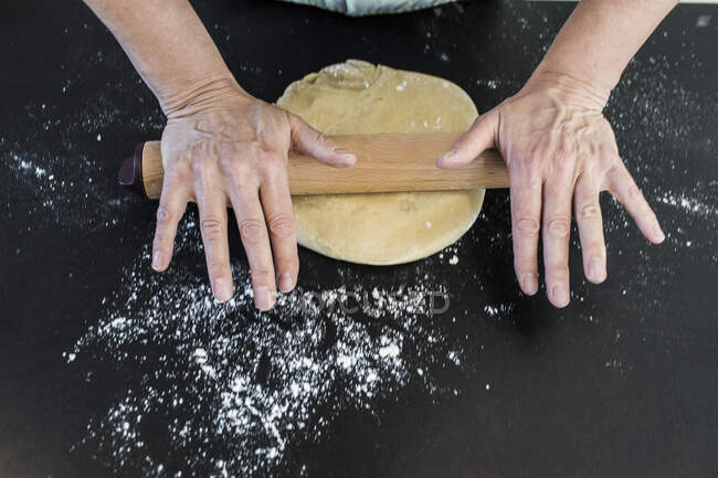 Женщина катит тесто со скалкой на мучном кухонном столе — стоковое фото