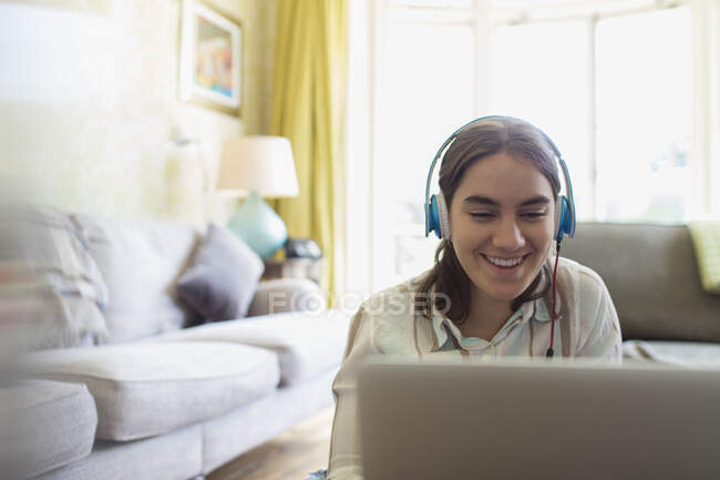 Усміхнена дівчина-підліток з навушниками, використовуючи ноутбук у вітальні — стокове фото