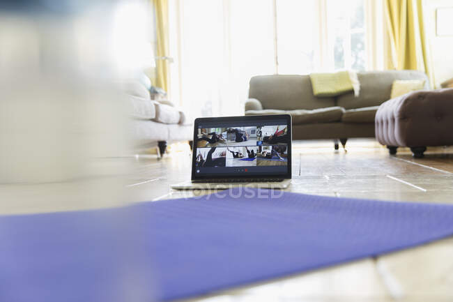 Clase de ejercicio streaming en la pantalla del portátil detrás de la esterilla de yoga - foto de stock
