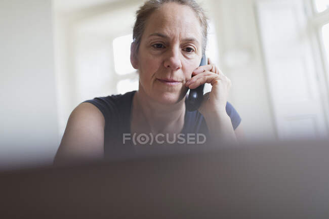 Mujer hablando por teléfono y trabajando en el portátil - foto de stock