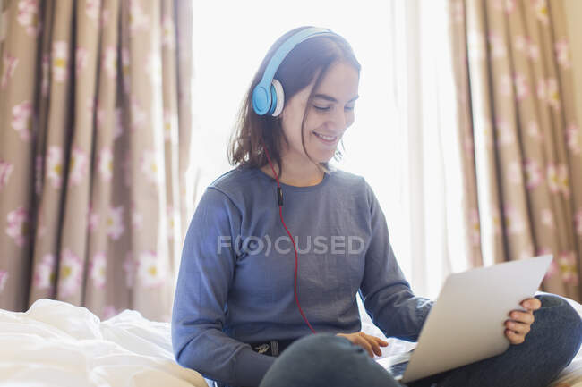 Ragazza adolescente con cuffie e laptop video chatta sul letto — Foto stock