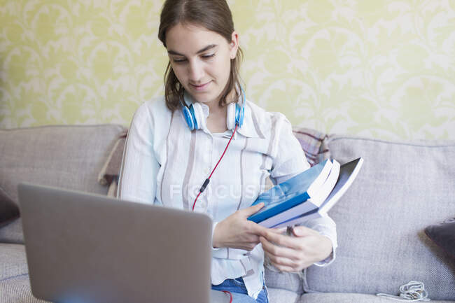 Adolescente avec livres et ordinateur portable à la maisonscolarisation sur canapé — Photo de stock