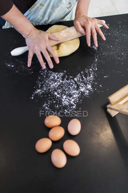 Женщина катит тесто на кухонном столе — стоковое фото