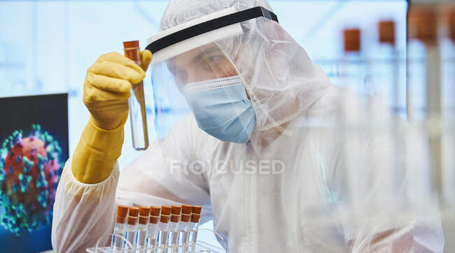 Científico masculino enfocado con tubo de ensayo investigando coronavirus - foto de stock