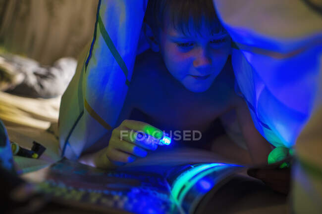 Хлопчик з журналом читання чорного світла під ковдрою — стокове фото